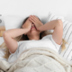 Frau im Bett hält sich die Augen zu während der Wecker klingelt